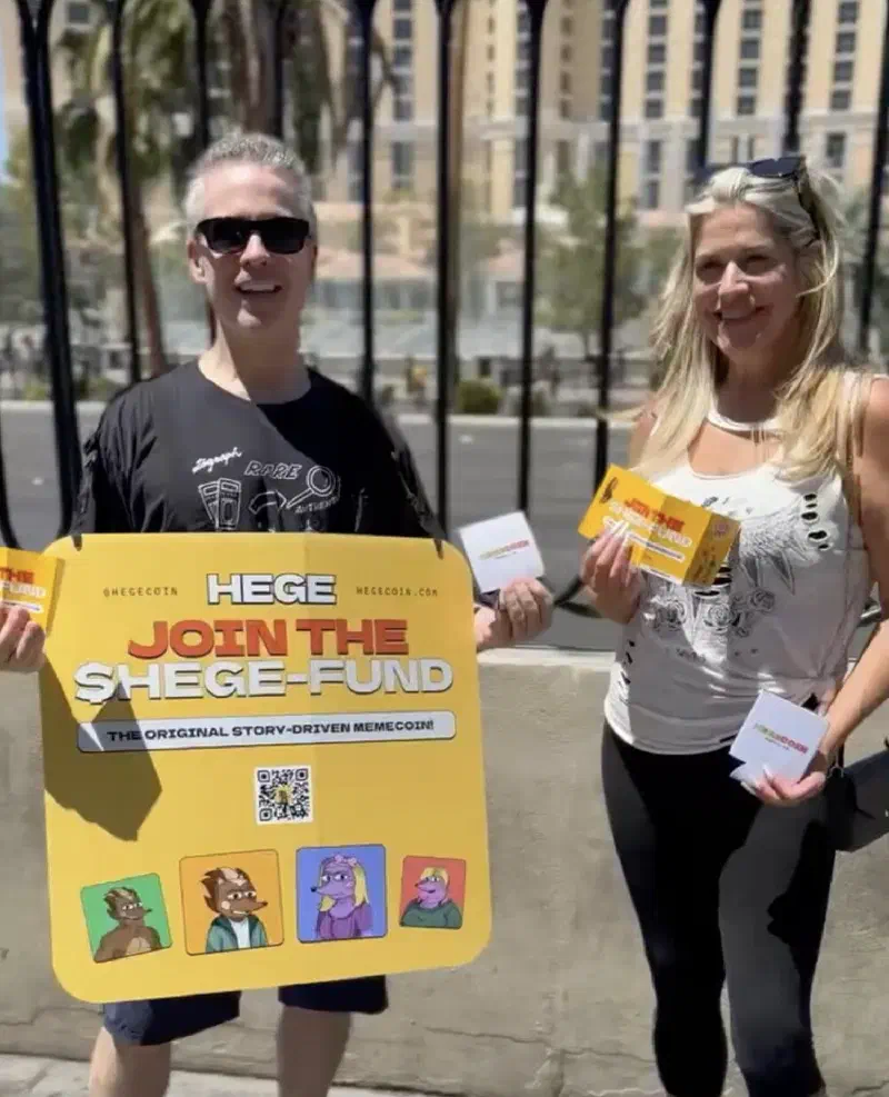 A man and a woman standing on a street i Las Vegas, holding up HEGE promotional material
