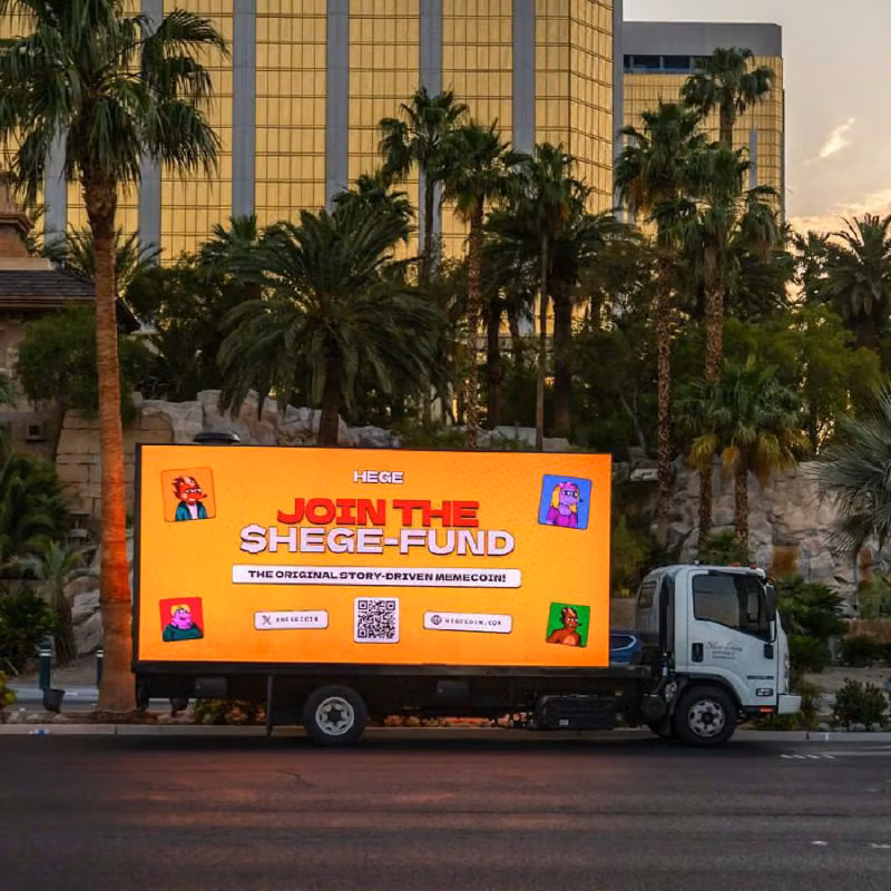 Sideways view of a truck displaying a large HEGE ad on its side, with palm trees and the glassy exterior of a hotel in the background
